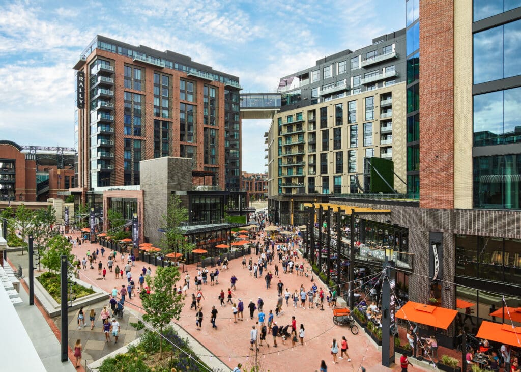 The exterior of The Rally Hotel in Denver with high rise buildings and people walking throughout the shopping area. 