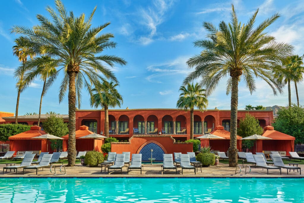 An exterior view of Omni Scottsdale Resort & Spa at Montelucia guest rooms and pool area with loungers and palm trees.