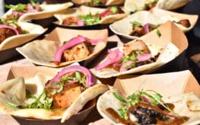 Several cardboard food containers with garnished chicken and red onion at the Devour Culinary Classic.