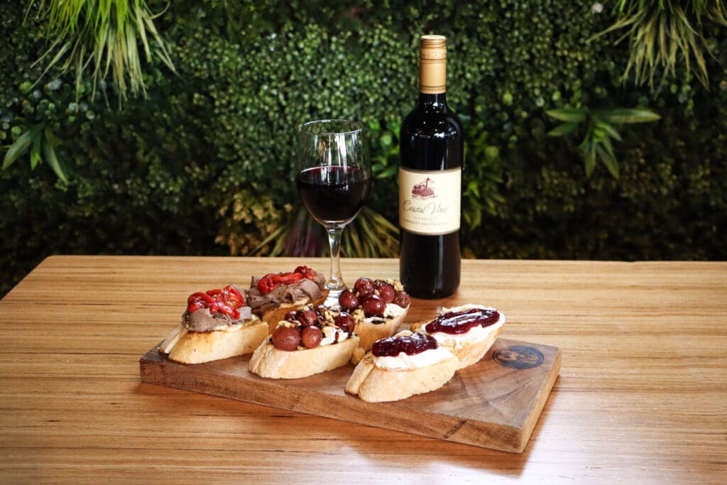 A platter of sliced bruschetta bread and toppings with a wine glass and wine bottle at 32 Shea.