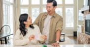 An Asian man and woman couple, work together on a craft in their kitchen.