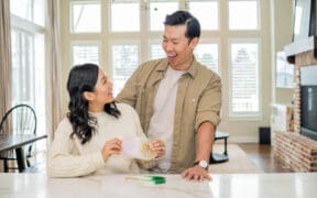 An Asian man and woman couple, work together on a craft in their kitchen.