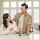 An Asian man and woman couple, work together on a craft in their kitchen.