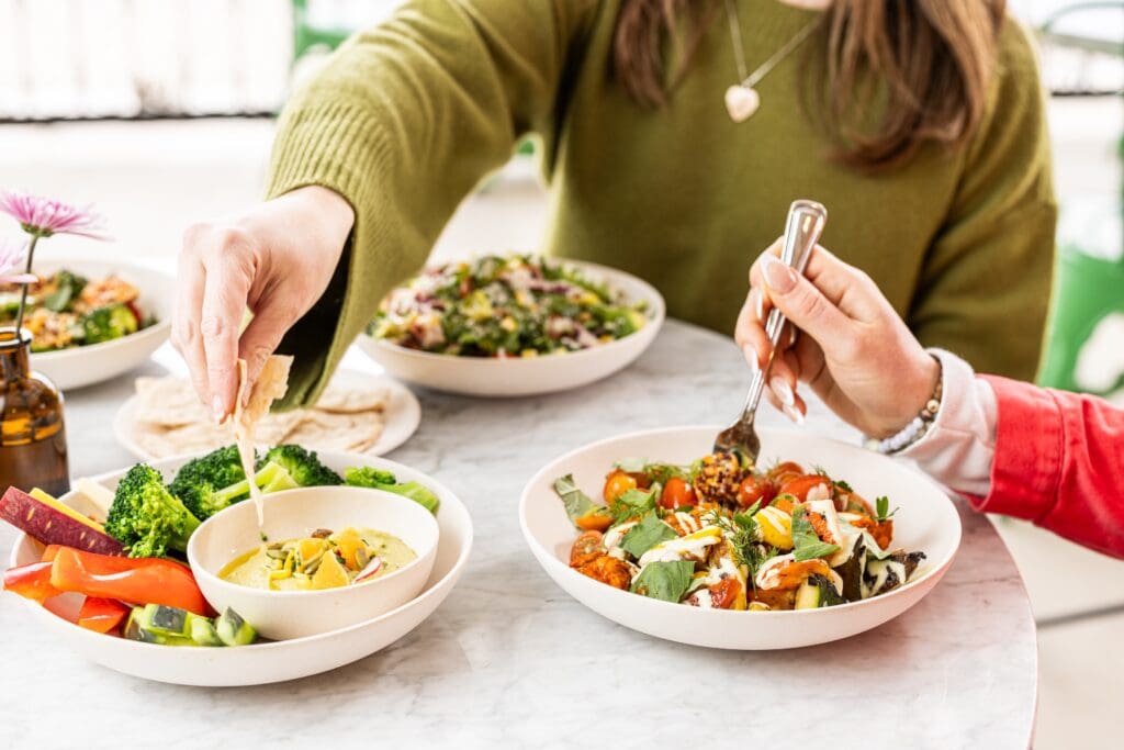 Two friends share bowls and salads with lettuce, tomato and other healthy foods from Flower Child.