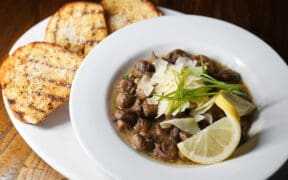 A bowl of bean soup garnished with slices of lemon and shaved parmesan with toasted bread on the side.