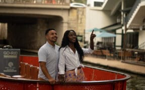 A black couple embraces, looking over the San Antonio River Walk.