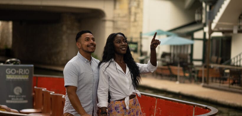 A black couple embraces, looking over the San Antonio River Walk.