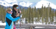A man and woman with ski poles in Grand County Colorado on a mountain with trees and snow.