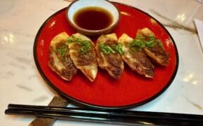 Tiki Taka's Gyoza on a plate next to chopsticks with a small bowl ofsherry dip.