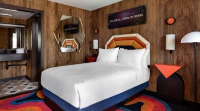 Guest room with a queen-size bed and funky swirly carpet and 70's retro decor with open access to the bathroom at at The Americana Motor Hotel in Flagstaff.