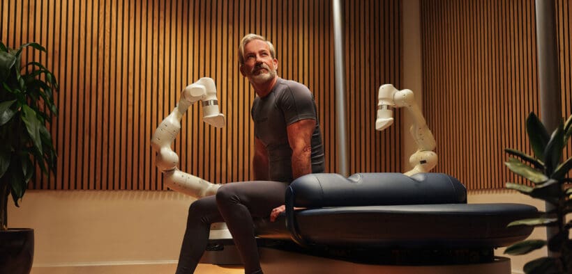 A man sits on a massage table at the AWAY Spa at W Scottsdale next to the Aescape AI massage tool.
