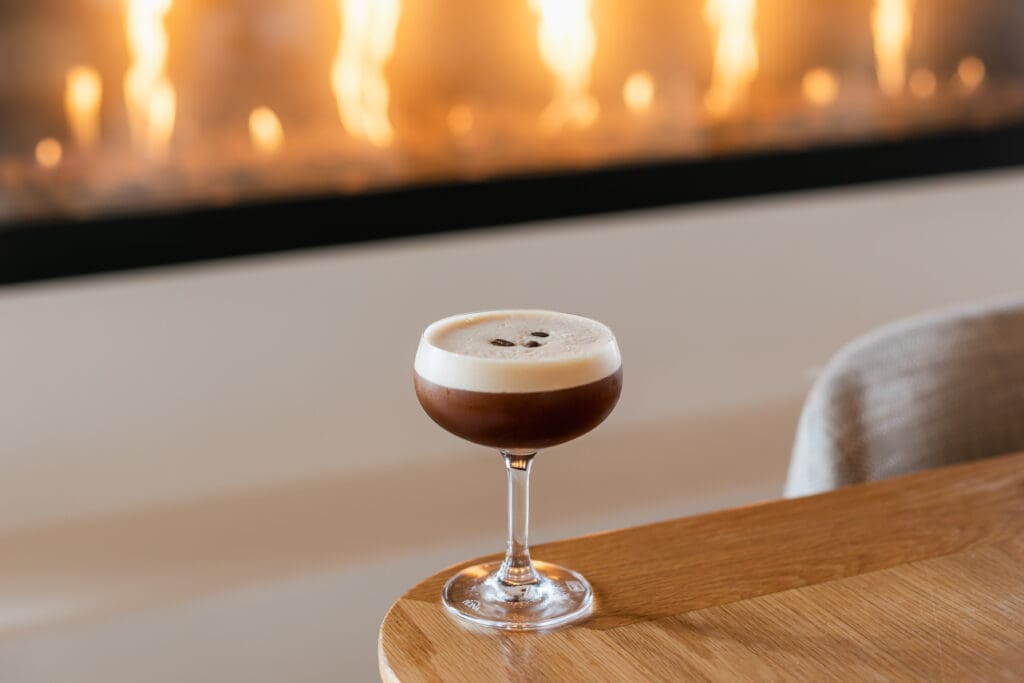An espresso martini on a table next to a fire at Covewood San Diego Mission Bay Resort.