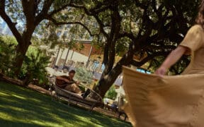 A man plays guitar and a woman dances in a flowing dress at the Four Seasons Hotel Austin lawn area.
