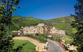 The Montage Deer Valley resort surrounded by forestry and a mountainscape with a road leading into the property.