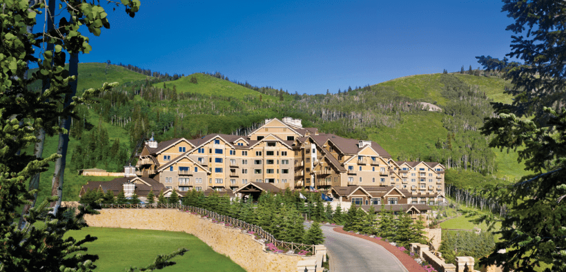 The Montage Deer Valley resort surrounded by forestry and a mountainscape with a road leading into the property.