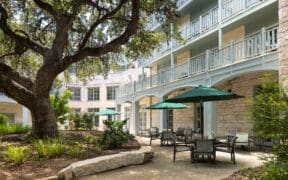 The Springhouse Cafe with outdoor umbrellas outside of the Hyatt Regency Hill Country Resort with large tree and landscaping