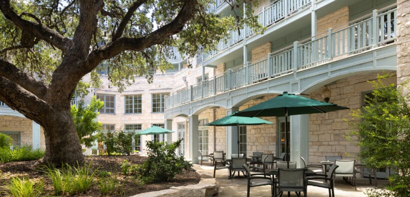 The Springhouse Cafe with outdoor umbrellas outside of the Hyatt Regency Hill Country Resort with large tree and landscaping