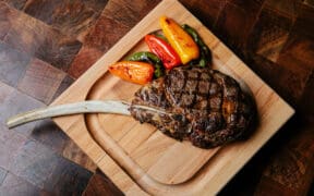 A Tomahawk steak and peppers on a cutting board at J&G Steakhouse at The Phoenician