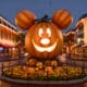 A big lit up pumpkin head of Mickey Mouse in the center of Main Street Disneyland surrounded by lit up shops.