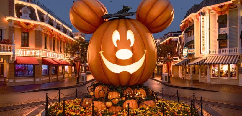 A big lit up pumpkin head of Mickey Mouse in the center of Main Street Disneyland surrounded by lit up shops.