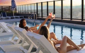 Two women in Adorandak chairs toast each other with cocktails on the Rose & Thorn restaurant atop the Penrose.