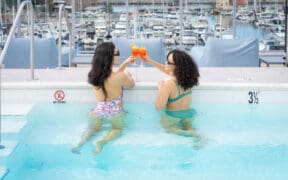 Two women in Shade at the Marina are toasting cocktails in a pool overlooking the marina at Redondo Beach.