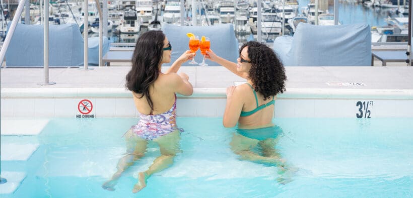 Two women in Shade at the Marina are toasting cocktails in a pool overlooking the marina at Redondo Beach.