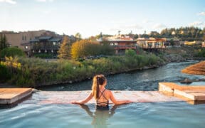A woman in a bathing suit and ponytail is in geothermal plunge pool at The Springs Resort and Spa, looking over the San Juan River.