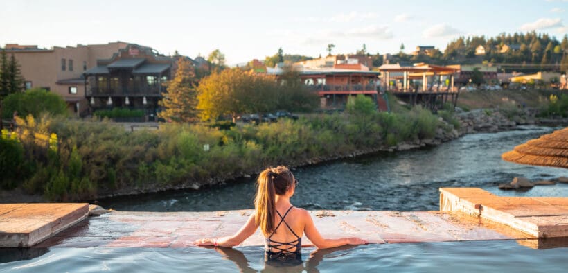 A woman in a bathing suit and ponytail is in geothermal plunge pool at The Springs Resort and Spa, looking over the San Juan River.