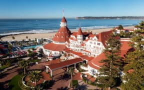 An aerial view of Hotel Del Coronado with its turrets and main drive and pool area next to the Pacific Ocean.