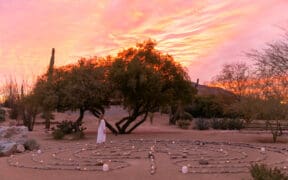 A woman walks the CIVANA Wellness Resorts, rock meditation path in a spiral at sunset.