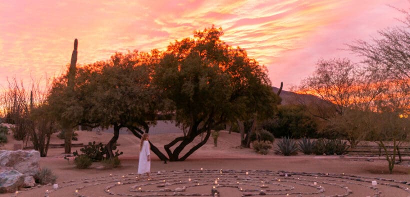 A woman walks the CIVANA Wellness Resorts, rock meditation path in a spiral at sunset.