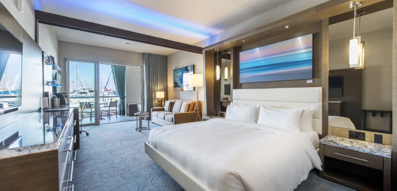 A Shade at the Marina Redondo Beach Deluxe King room with comfy bed, dresser, couch and balcony views of the marina.