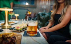 A woman sits in front of a plate of appetizers and a cocktail at The Peacock at DC Ranch speakeasy.