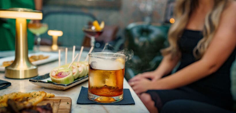 A woman sits in front of a plate of appetizers and a cocktail at The Peacock at DC Ranch speakeasy.