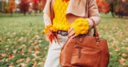 Close up of a stylish woman holding a fall bag wearing a sweater in autumn park.