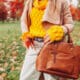 Close up of a stylish woman holding a fall bag wearing a sweater in autumn park.