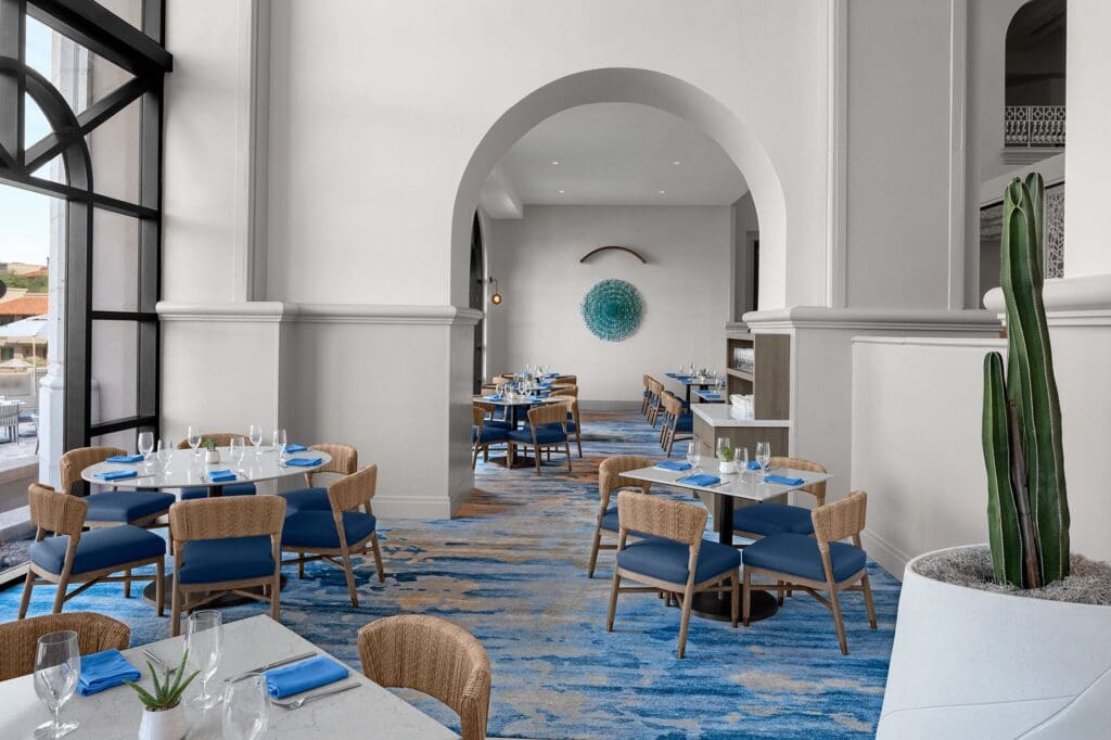 The expansive dining room at La Luz in Tucson with round and square tables and seating next to a big picture window.