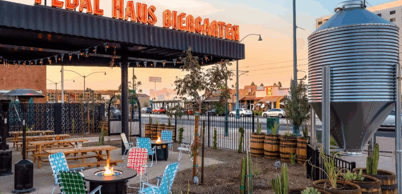 The outdoor view of Pedal Haus Brewery in Mesa with seating, a firepit and decorative barrels with plants.
