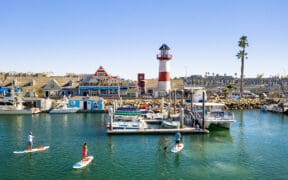 Oceanside Harbor with sailboats, lighthouse and paddle boarders in the bay.