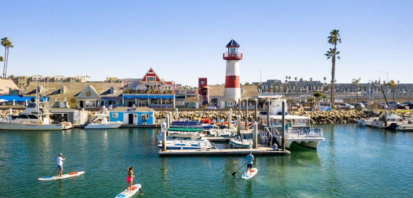 Oceanside Harbor with sailboats, lighthouse and paddle boarders in the bay.
