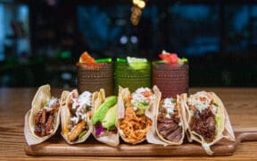 A plate of different types of tacos at Salt + Lime Modern Mexican Grill in Arcadia with three cocktails in the background.