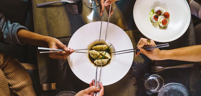 Group of people sharing Chinese steamed dumpling, view of the table with four hands holding chopsticks on fusion food luxury restaurant.