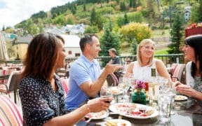 A group of people sit at an outdoor dining spot in Park City with a view of the surrounding mountains.