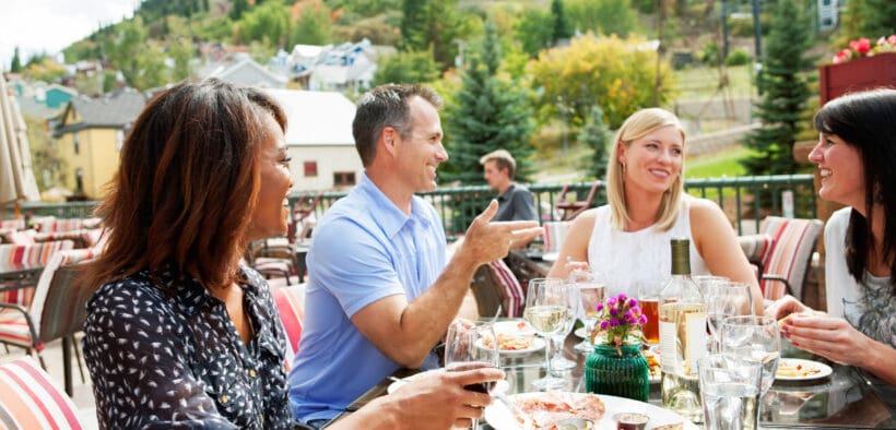 A group of people sit at an outdoor dining spot in Park City with a view of the surrounding mountains.