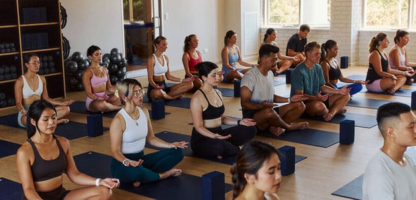A full class of people in lotus position in a Mindbody and CorePlus pilates class.