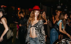 A model at Scottsdale Fashion Week wears a red fedora, zebra print cover up, bra top and jeans.
