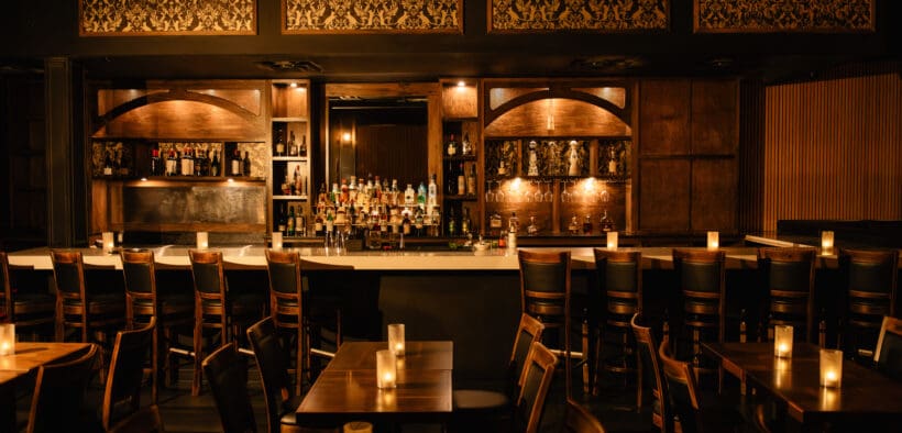 A prohibition decored bar with dark lighting and oak wood accents and seating at Nica on 4th in Downtown Austin.