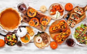 A smattering of pumpkin-themed dishes; pumpkin pie, pumpkin dip, stuffed pumpkins and squash salad on a wood table.