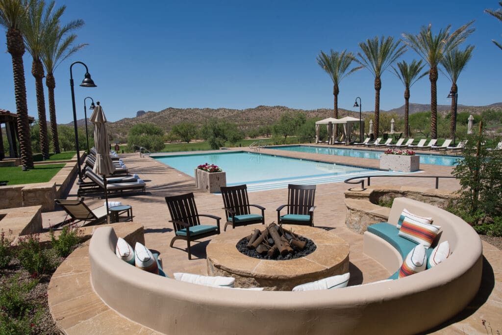 Chairs surrounding a firepit with comfy seating and a pool and palm trees at Rancho de los Caballeros.
